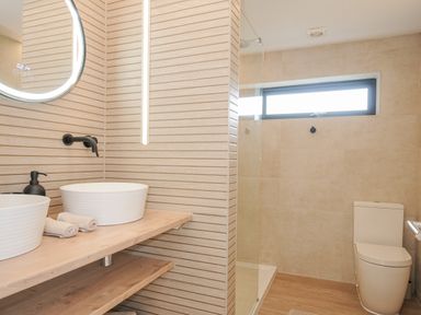 A bathroom with two white sinks on a wooden countertop a round mirror a walk-in shower and a toilet at 100 Hillside Villas in Looe