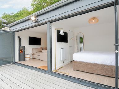 A bedroom with a bed and mirror next to a living room with a sofa and stove at 100 Hillside Villas in Looe