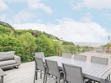 A patio with a table and chairs overlooking trees and hills near the coast at 100 Hillside Villas in Looe