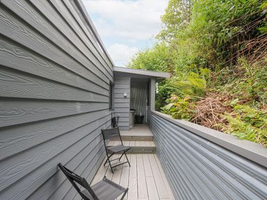 A narrow outdoor deck with two folding chairs and grey wood paneling at 100 Hillside Villas in Looe