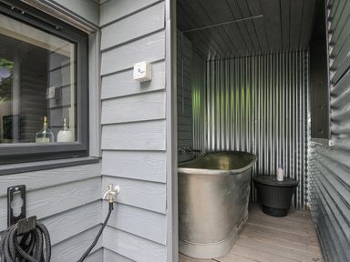 An outdoor space with a metal bathtub surrounded by corrugated metal walls and a small table with a bottle at 100 Hillside Villas in Looe