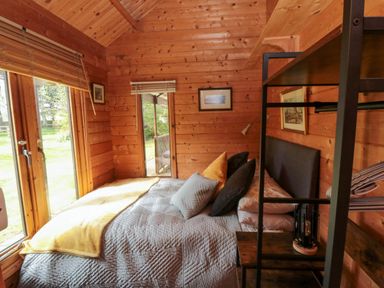 A wooden bedroom with a bed pillows blankets a metal shelf and a glass door at Snape Castle Garden Lodge Snape near Bedale