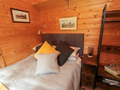 A bedroom with a bed with multiple pillows and wooden walls at Snape Castle Garden Lodge in Snape near Bedale