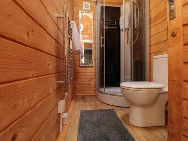 A bathroom with wooden walls featuring a toilet shower enclosure mirror and towel rack at Snape Castle Garden Lodge Snape near Bedale