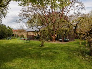 A garden with green grass trees outdoor seating and a covered patio at Snape Castle Garden Lodge in Snape near Bedale