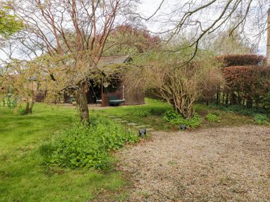 A garden with trees a wooden shed a gravel parking area and a metal table and chairs at Snape Castle Garden Lodge in Snape near Bedale