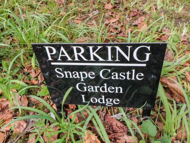 A black parking sign with white text placed in grass and fallen leaves at Snape Castle Garden Lodge Snape near Bedale