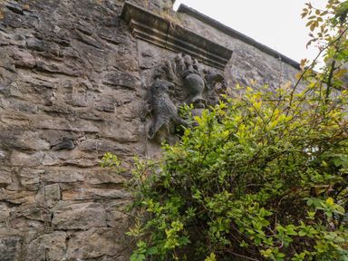 A stone wall with a carved coat of arms partially covered by green foliage at Snape Castle Garden Lodge in Snape near Bedale