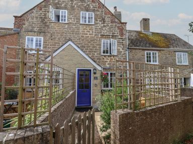 Stone cottage with blue door and trellis fences enclosing a small garden at Old Ropemakers Cottage in Bridport