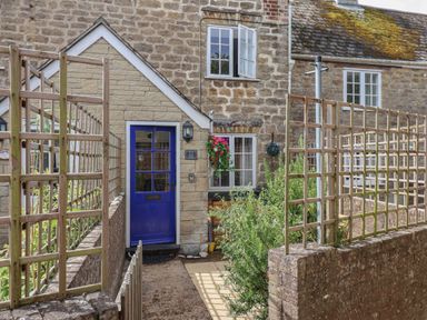 An exterior view of a stone cottage with a blue door and wooden trellis fencing at Old Ropemakers Cottage in Bridport
