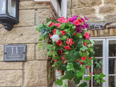 A hanging basket with colorful flowers on the exterior wall of a stone building at The Old Ropemakers Cottage in Bridport