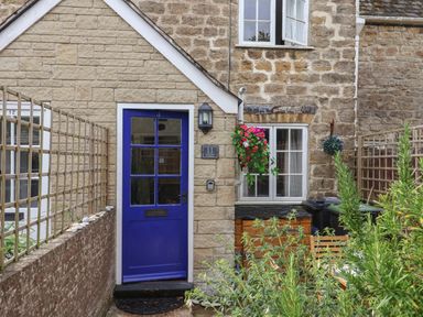 Front door with blue paint on a stone cottage with potted plants and wooden fence at Old Ropemakers Cottage in Bridport