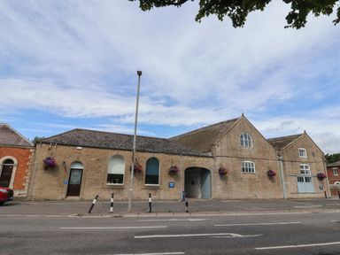A street view of a stone building with arched windows and doors with hanging flower baskets at Old Ropemakers Cottage in Bridport