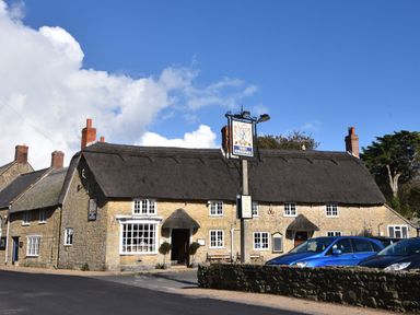 A thatched roof pub building with a signpost and parked cars in front at Old Ropemakers Cottage in Bridport