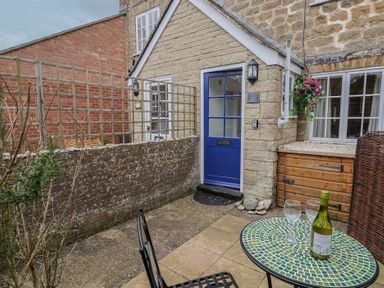 A small outdoor patio area with a blue door in a stone building and a table with a bottle and two glasses at Old Ropemakers Cottage in Bridport