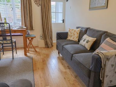 A living room with a gray sofa with patterned cushions and a dining table with chairs near a window at Old Ropemakers Cottage Bridport