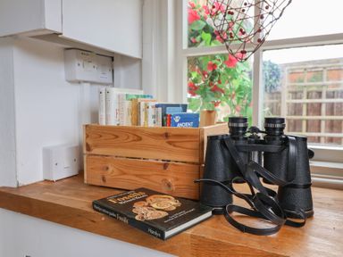 A wooden crate with books next to binoculars and a book on fossils on a wooden windowsill at Old Ropemakers Cottage in Bridport