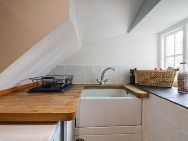 A kitchen sink with wooden countertop a dish rack a woven basket and a glass jar by a window at Old Ropemakers Cottage in Bridport