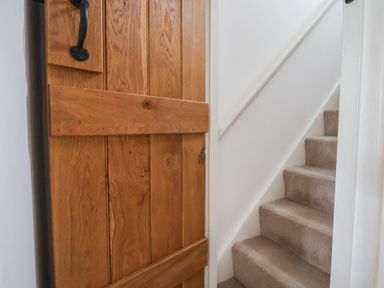 A wooden door partially open next to carpeted stairs with a white handrail at Old Ropemakers Cottage Bridport
