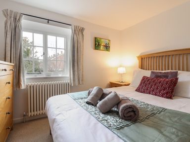 A bedroom with a double bed rolled towels on the bed a bedside table with a lamp a chest of drawers and a window with curtains at Old Ropemakers Cottage in Bridport