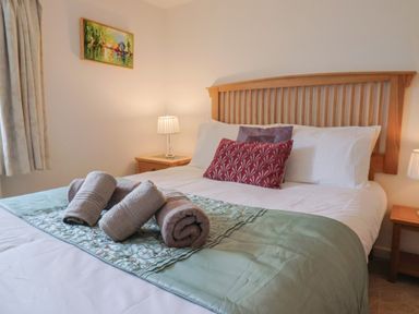 A bedroom with a wooden bed frame bedside tables with lamps rolled towels on bed at Old Ropemakers Cottage in Bridport