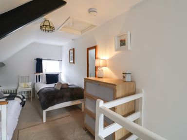 A bedroom with two single beds a chest of drawers a chair and a lamp at Old Ropemakers Cottage in Bridport