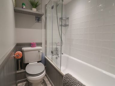 A bathroom with a toilet next to a bathtub with a shower and white tiled walls at Old Ropemakers Cottage in Bridport