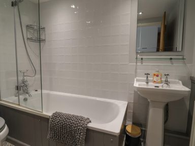 A bathroom with a bathtub a shower a sink with soap and a small trash can at Old Ropemakers Cottage in Bridport
