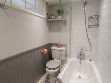 A bathroom with a toilet next to a bathtub with a shower and a glass partition at Old Ropemakers Cottage in Bridport