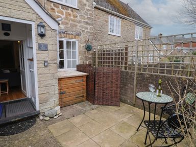A small outdoor patio with a mosaic table and two wrought iron chairs outside a stone cottage at Old Ropemakers Cottage in Bridport