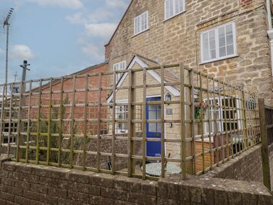 An exterior view of a stone building with a blue door behind a wooden lattice fence at Old Ropemakers Cottage in Bridport