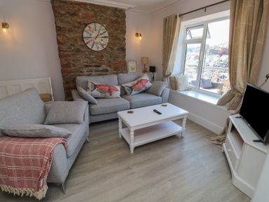 A living room with two gray sofas a white coffee table a TV on a stand and a window with a view at Fishnets in Brixham