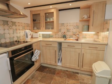 A kitchen with wooden cabinets a stove an oven a white kettle a toaster a sink and tiled backsplash at Fishnets in Brixham