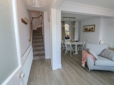 A hallway with stairs leading up and a view into a dining area with round table and chairs and a living space with a sofa at Fishnets in Brixham