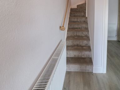 A narrow carpeted staircase with a rope handrail and a radiator on the left wall at Fishnets in Brixham