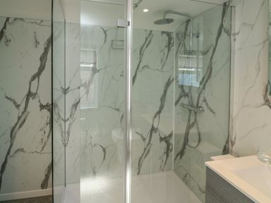 A bathroom shower area with glass doors marble patterned walls and a mounted showerhead at Fishnets in Brixham