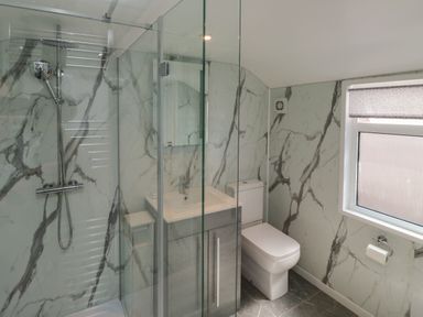 A bathroom with a glass shower enclosure a sink with a vanity unit a toilet and a window with a roller blind at Fishnets in Brixham