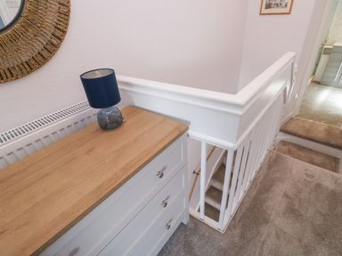 A hallway with a white drawer unit topped with a blue lamp next to a white staircase railing at Fishnets in Brixham