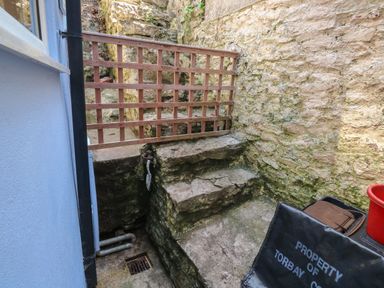 A small stone outdoor area with stairs a wooden gate and a black chair at Fishnets in Brixham
