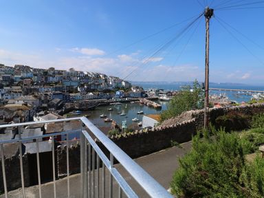 A view of a harbor with boats water and houses on a hillside behind a metal railing and a stone wall at Fishnets in Brixham