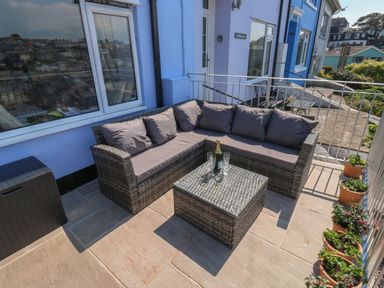 A patio with a sectional sofa a glass top table and potted plants at Fishnets in Brixham
