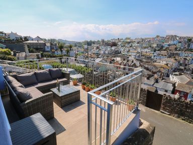 A balcony with outdoor seating and potted plants overlooking a town at Fishnets in Brixham