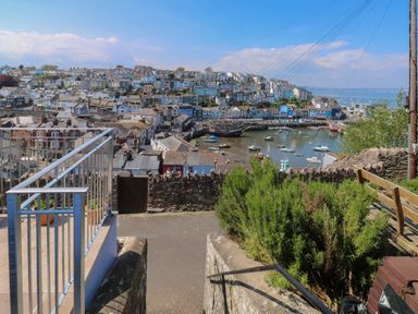 A view of a coastal town with numerous houses overlooking a harbor with boats and a stone wall with bushes in the foreground at Fishnets in Brixham