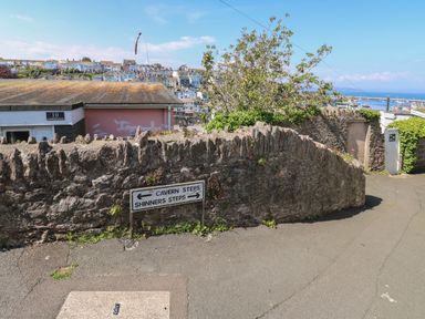 A street view with a stone wall and directional signs for Cavern Steps and Shinners Steps with houses and a harbor in the background at Fishnets in Brixham