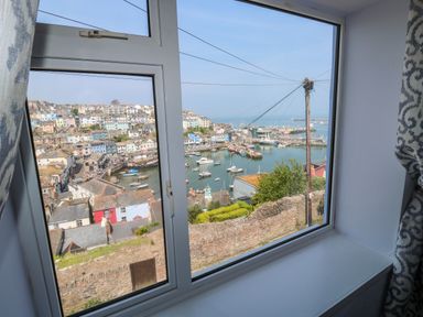 View of a harbor with boats and houses on a hillside through a window with patterned curtains at Fishnets in Brixham