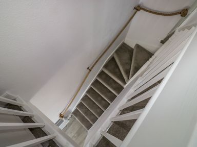 A carpeted staircase with white railings and a rope handrail on the wall at Fishnets in Brixham
