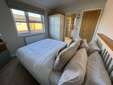 A bedroom with a bed and pillows a wardrobe and a wooden door at Lodge 18 - The Pines in Runswick Bay