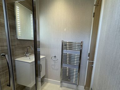 A bathroom with a sink and mirror on a tiled wall beside a chrome towel radiator at Lodge 18 - The Pines in Runswick Bay