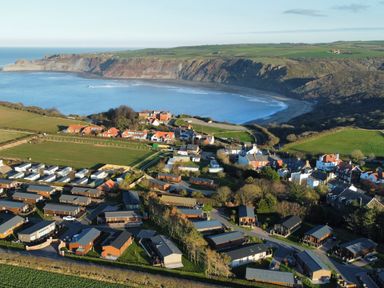 An aerial view of a coastal village with houses fields and a bay with cliffs at Lodge 18 - The Pines in Runswick Bay