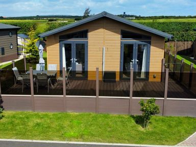 A wooden house with two glass doors opening onto a deck with a table and chairs at Lodge 18 - The Pines in Runswick Bay